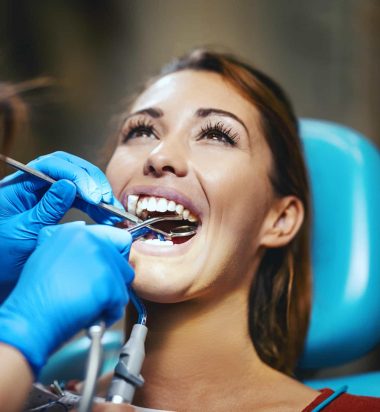 The beautiful young woman is at the dentist. She sits in the dentist's chair and the dentist sets braces on her teeth putting aesthetic self-aligning lingual locks.
